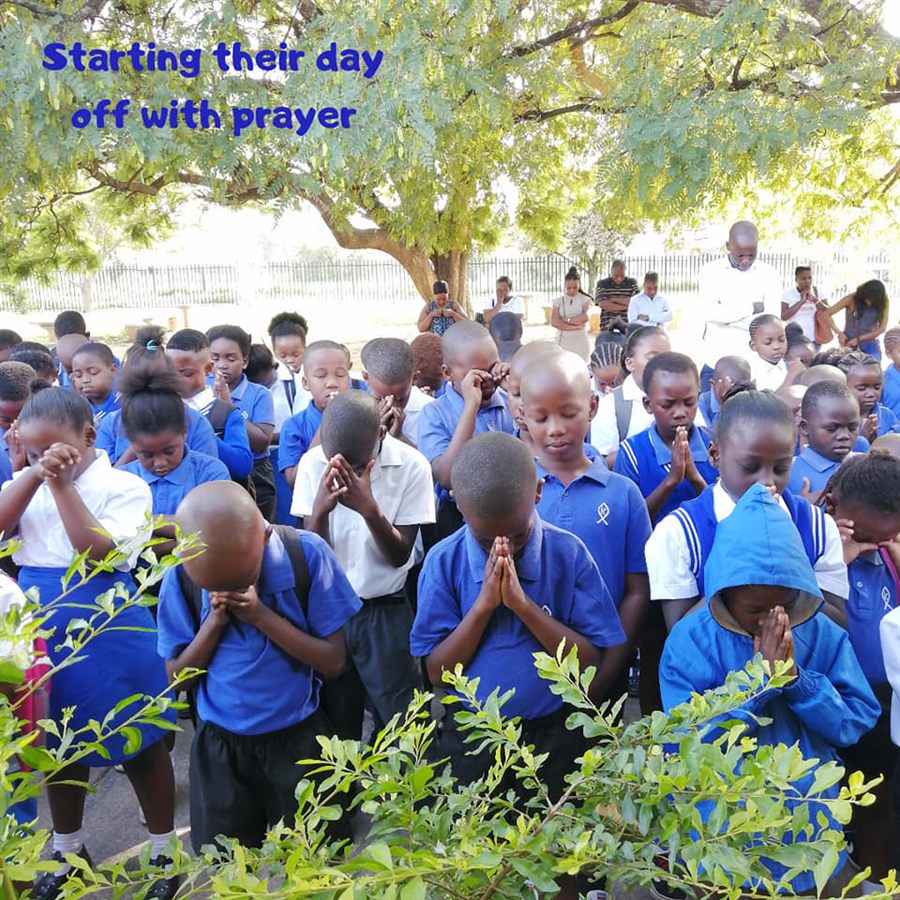 Kingsway learners in blue uniforms praying together under a tree